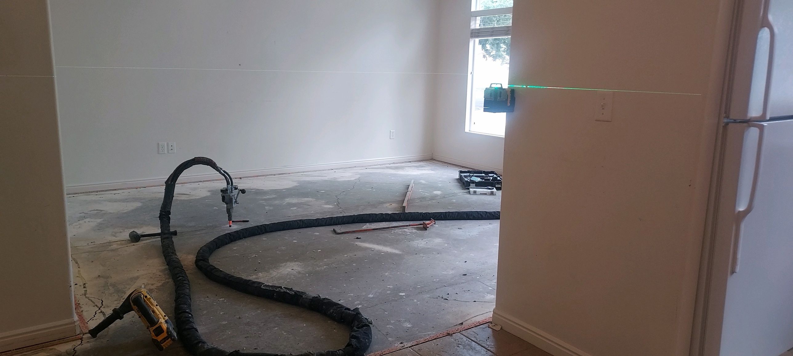 A green laser level marking grade across the wall while Poly-Lift raises an interior concrete slab with foam injection