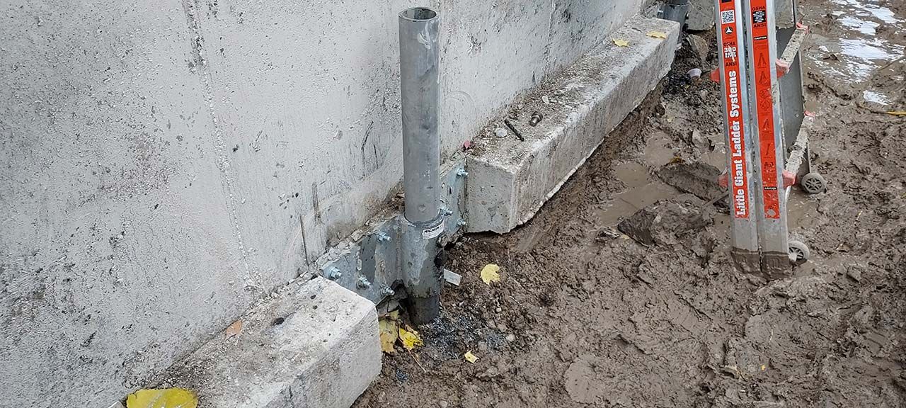 A steel push pier and bracket fastened to a concrete foundation footing on a Poly-Lift job
