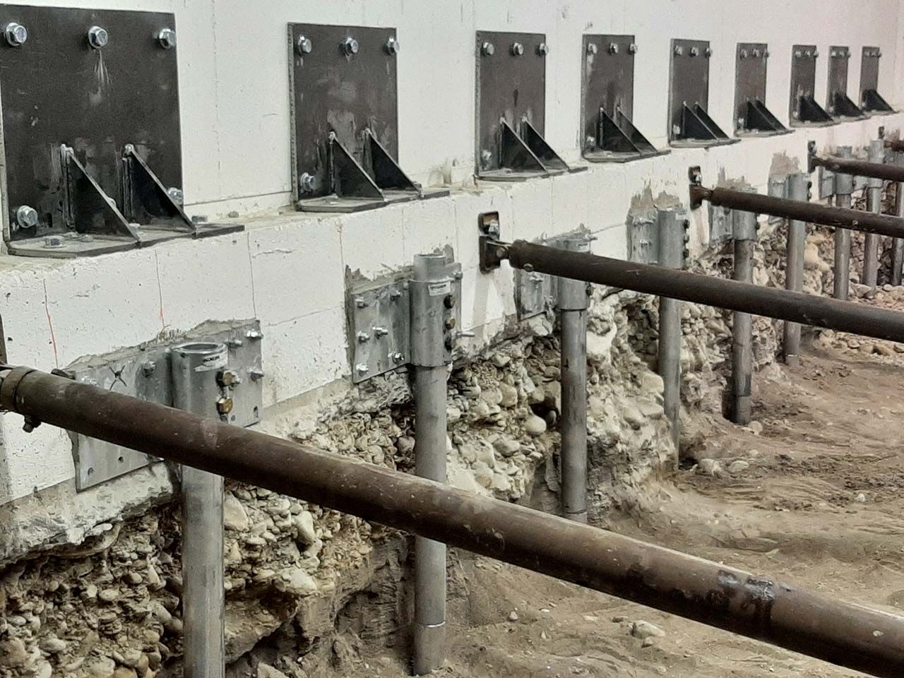 A row of steel push piers and lifting brackets along a foundation wall on a Poly-Lift piering job